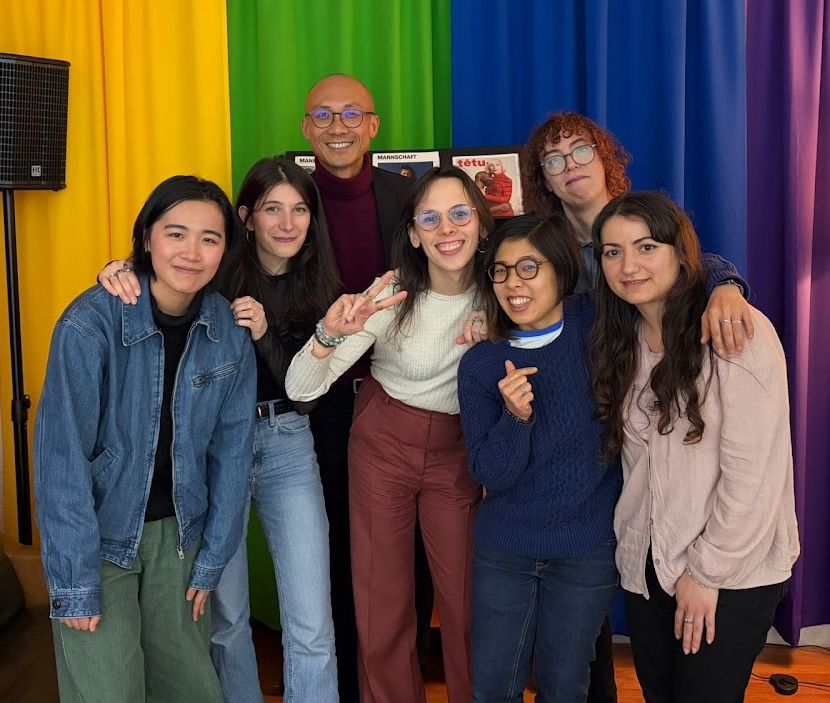 Seven members of Blom and CVRCLE Collective smiling together in front of rainbow curtains at the Rainbow Center