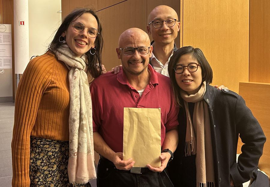 Three Blom members smiling with Dr. Erik Schneider of ITGL, who holds the envelope of donations collected at the ceremony