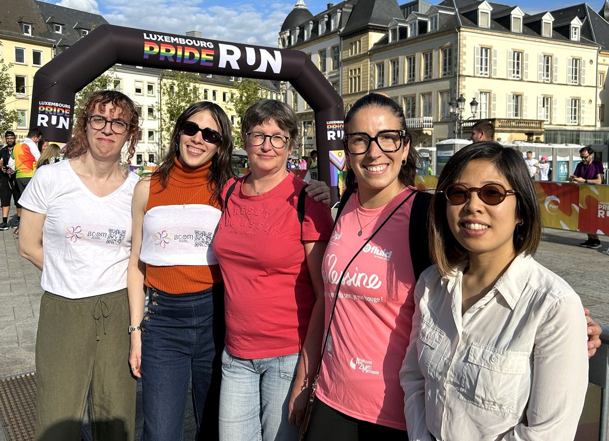 Five Blom and IMS members smiling in front of the Luxembourg Pride Run arch, two wearing Blom T-shirts