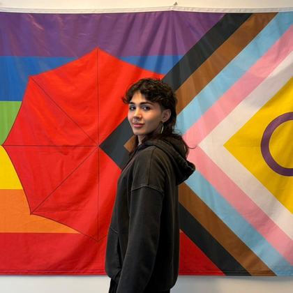 Portrait of Alex Shah in front of a progress pride flag